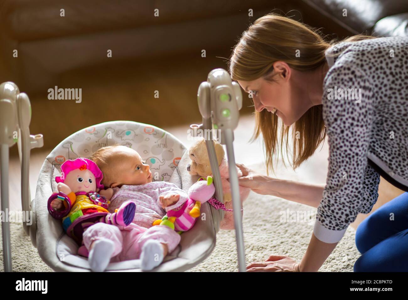 Femme jouant avec bébé entouré de jouets allongé dans balançoire de bébé Banque D'Images