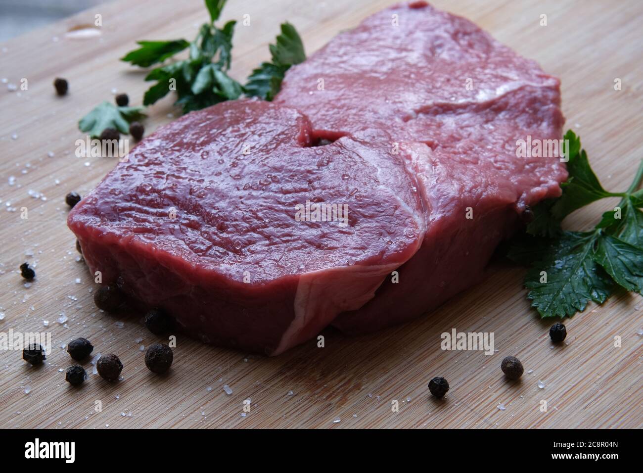 Steak de bœuf. Morceau de viande de bœuf mûre de 21 jours sur la table en bois de bambou avec du poivre noir et des cristaux de sel de mer. Banque D'Images