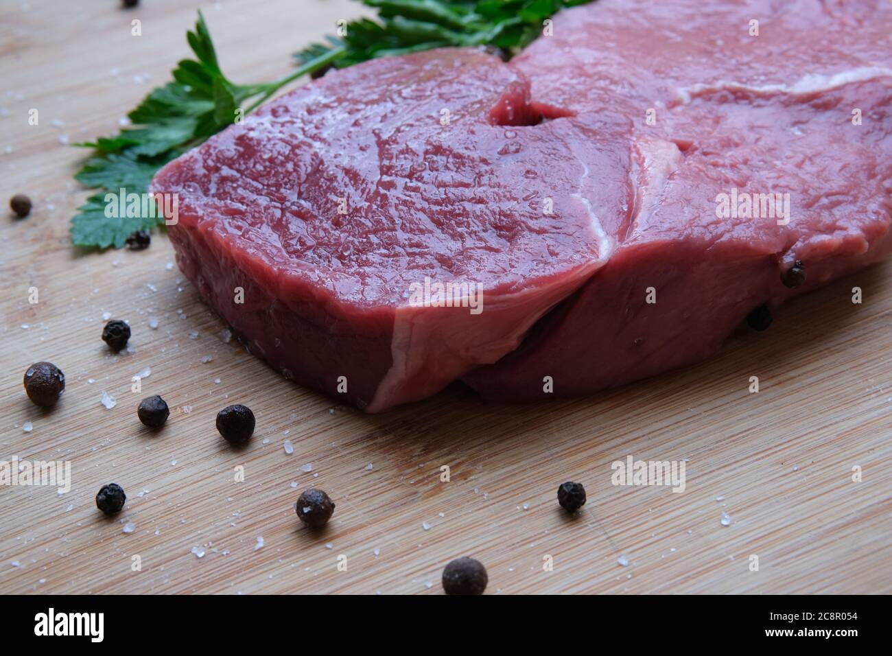 Steak de bœuf. Morceau de viande de bœuf mûre de 21 jours sur la table en bois de bambou avec du poivre noir et des cristaux de sel de mer. Banque D'Images