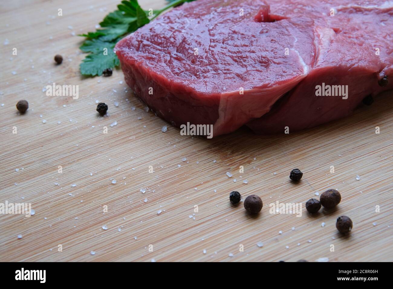 Steak de bœuf. Morceau de viande de bœuf mûre de 21 jours sur la table en bois de bambou avec du poivre noir et des cristaux de sel de mer. Banque D'Images