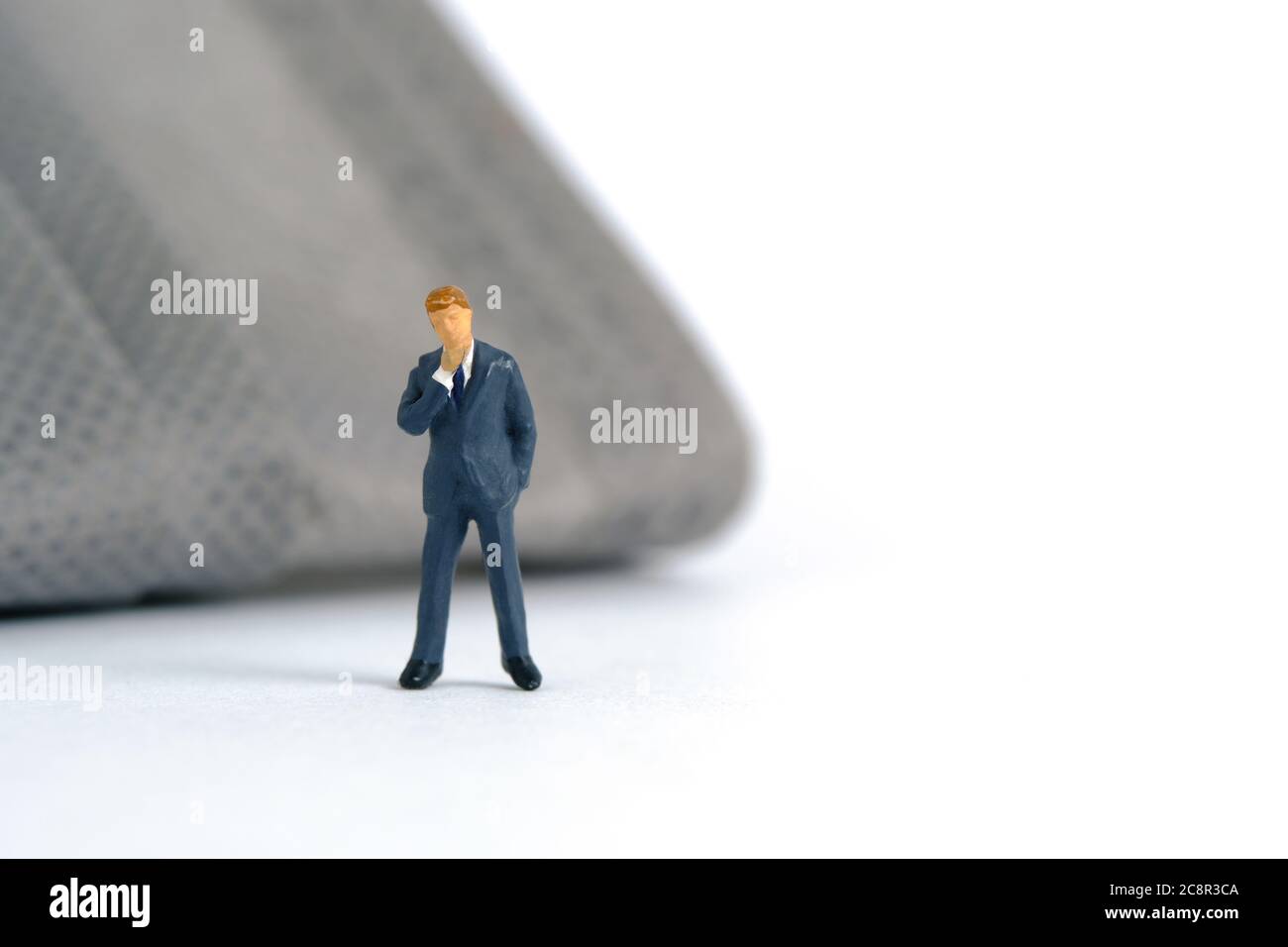 Photographie miniature conceptuelle du coronavirus pandémique – un homme d'affaires se tient devant un masque facial – comment porter un masque concept. Image photo Banque D'Images