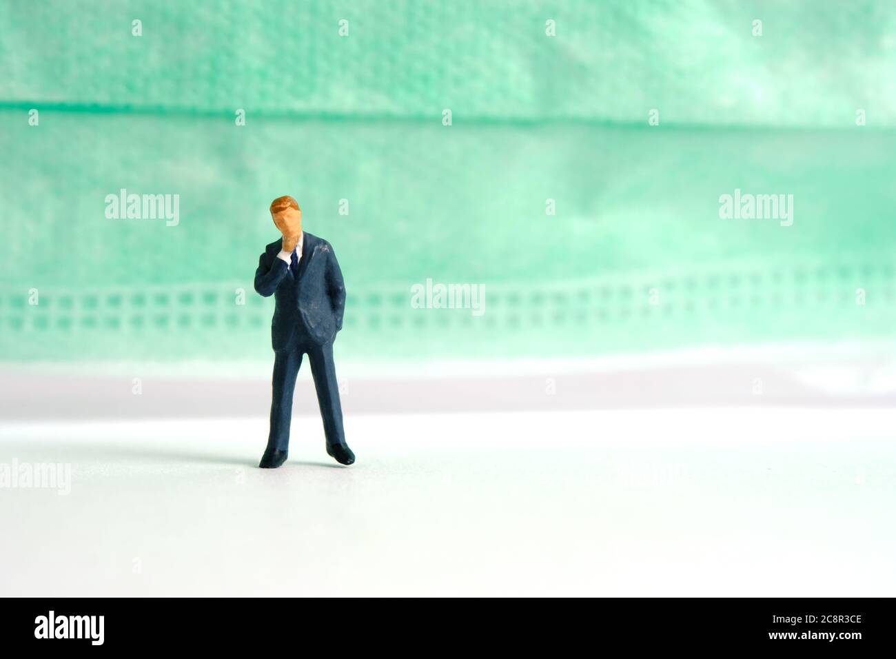 Photographie miniature conceptuelle du coronavirus pandémique – un homme d'affaires se tient devant un masque facial – comment porter un masque concept. Image photo Banque D'Images