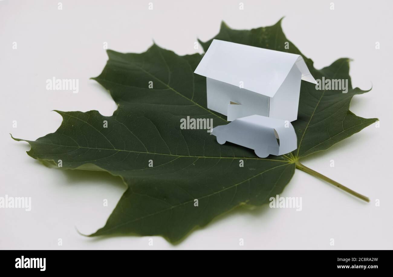 Une petite maison en papier et une voiture, toutes deux placées sur une feuille d'érable verte. Banque D'Images