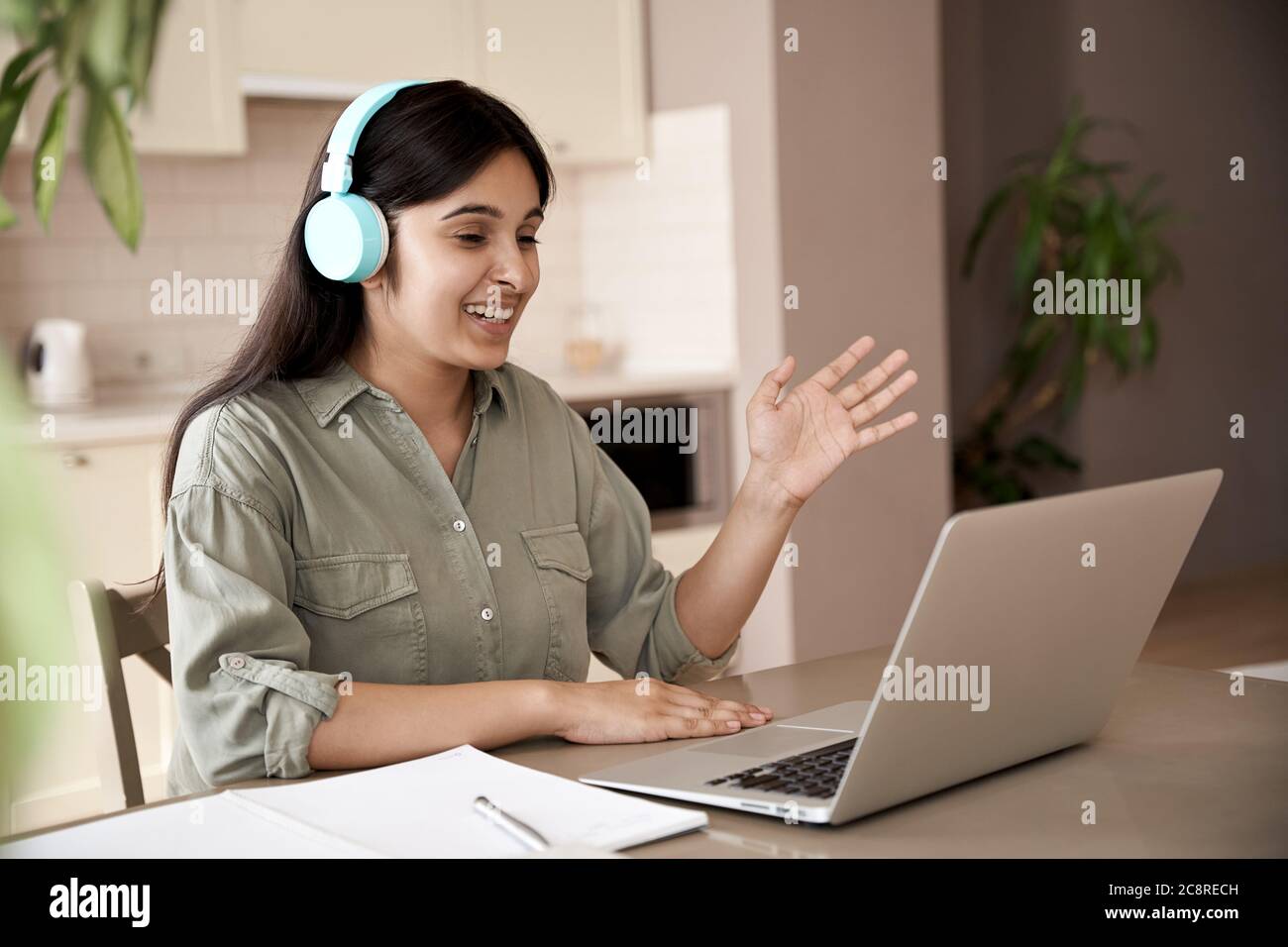 Bonne étudiante indienne portant un casque d'écoute pour les appels vidéo à la maison. Banque D'Images