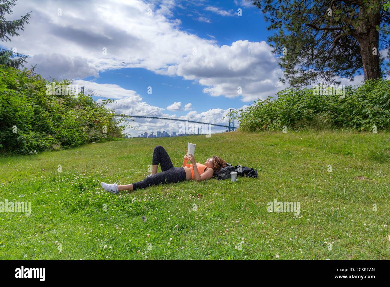 Une jeune femme allongé sur l'herbe lit un livre avec un pont en arrière-plan Banque D'Images
