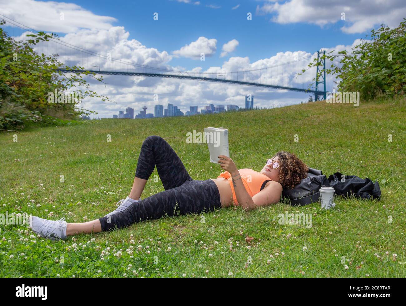 Une jeune femme allongé sur l'herbe lit un livre avec un pont en arrière-plan Banque D'Images