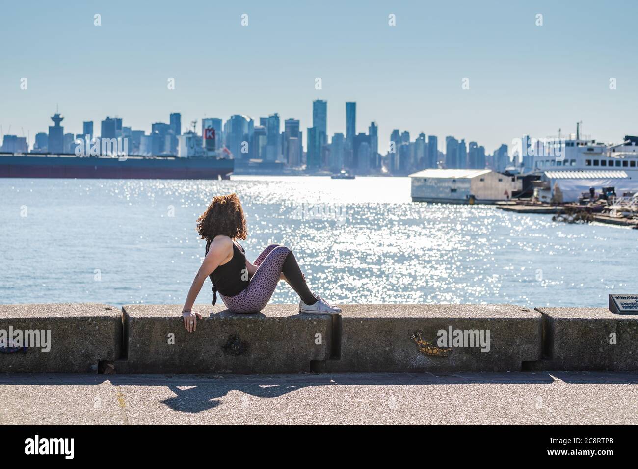 Une jeune femme fait du yoga sur la digue avec la ville de Vancouver en arrière-plan Banque D'Images