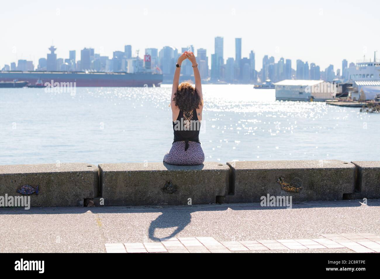 Une jeune femme fait du yoga sur la digue avec la ville de Vancouver en arrière-plan Banque D'Images