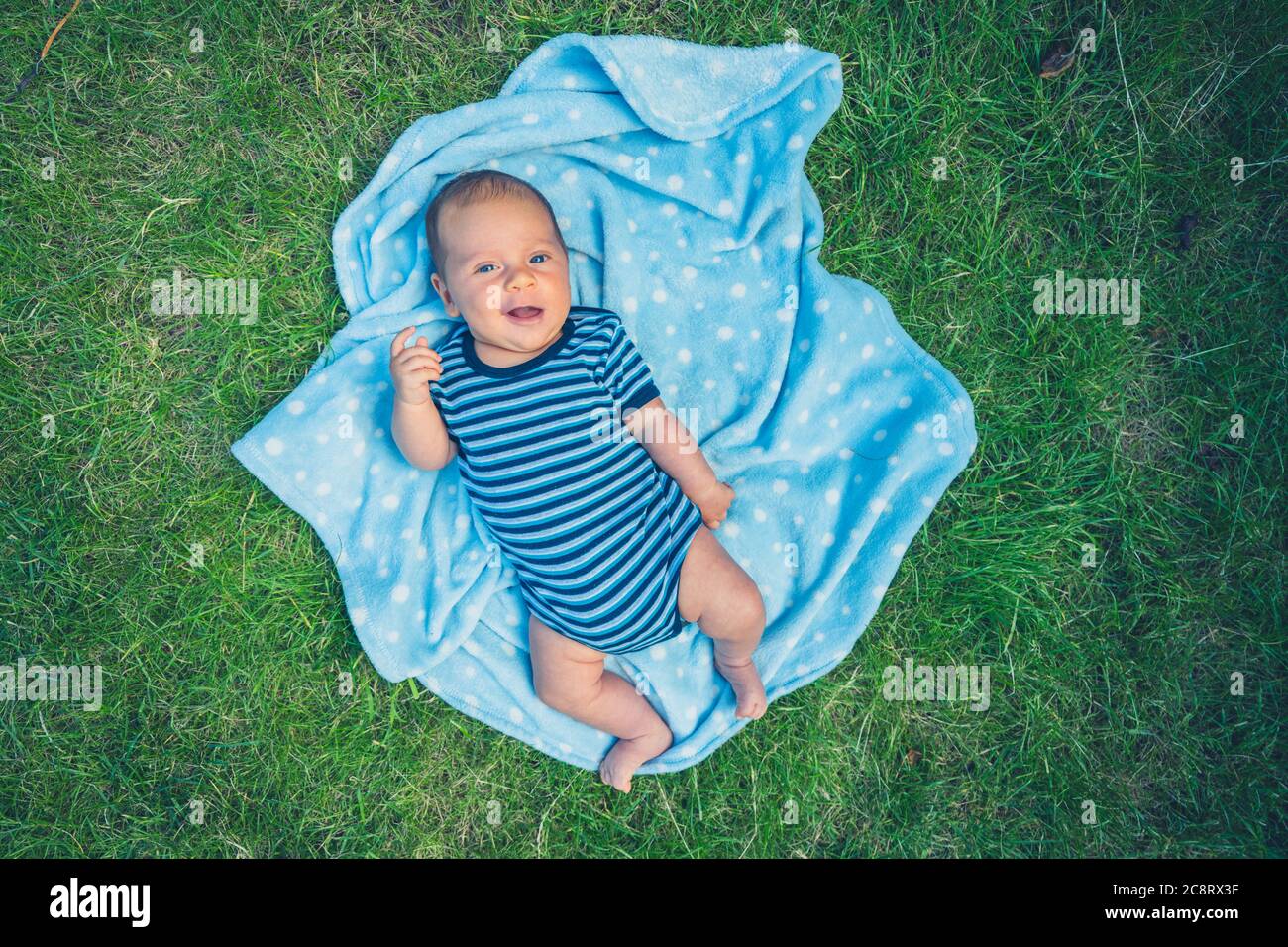 Un petit bébé est allongé sur une couverture sur la pelouse en été Banque D'Images