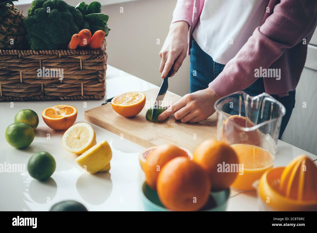 Femme caucasienne trancheuse des fruits pour faire du jus frais à la maison à l'aide d'un couteau Banque D'Images