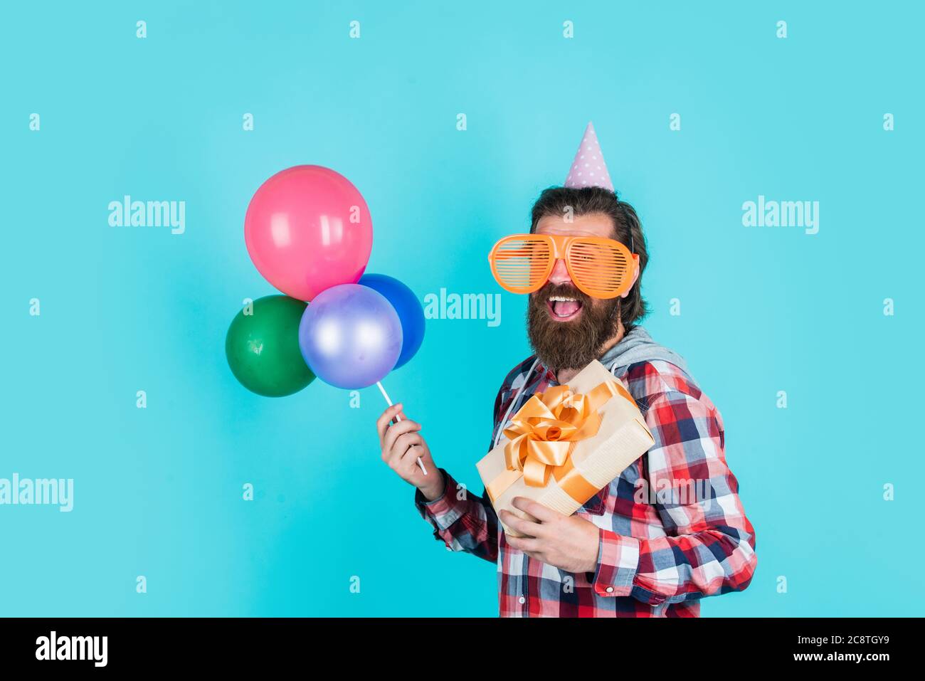 Quoi acheter. Gestionnaire d'événements avec boîte cadeau. Homme brutal en fête. Homme drôle en chapeau d'anniversaire. Joyeux Noël. Fête de la fête, fou. S'amuser avec des ballons. Préparez-vous pour un anniversaire. Banque D'Images
