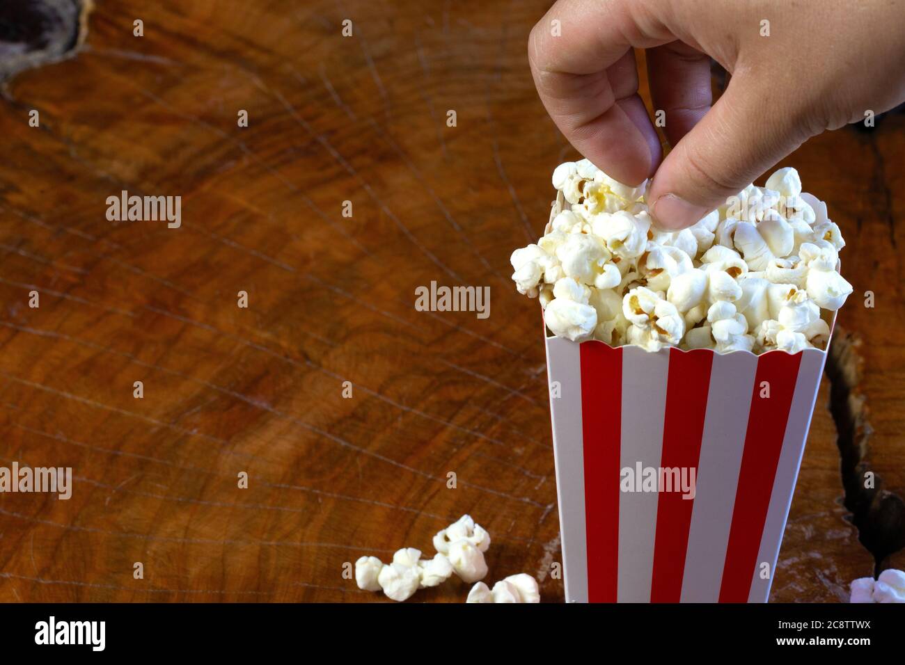 Main de pop-corn à retirer de rouge et blanc rayés en carton seau rétro conception sur table en bois Banque D'Images