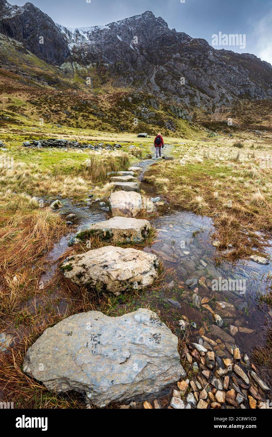 Des pierres qui traversent l'eau de fonte des montagnes enneigées de Glyder Fawr menant à Llyn Idwal, parc national de Snowdonia, au nord du pays de Galles Banque D'Images