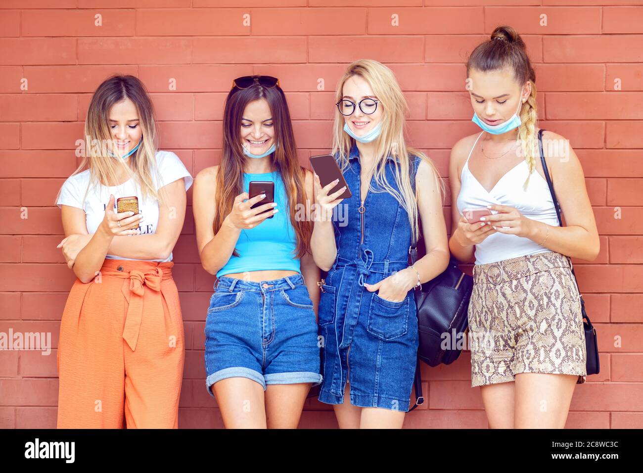 Jeunes filles avec masques de visage s'amusant en utilisant des téléphones mobiles en extérieur Banque D'Images