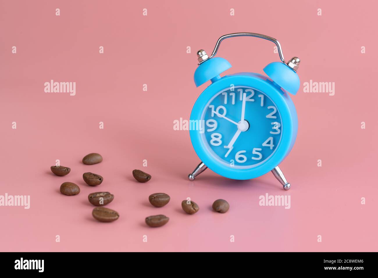 Réveil bleu et grains de café sur fond rose. Il est temps de se réveiller et de boire du café. Bonjour et début du nouveau concept de journée Banque D'Images