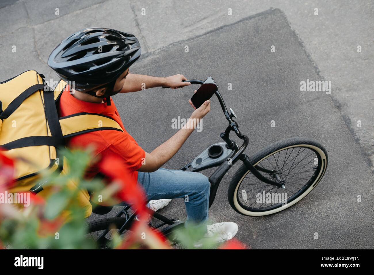 Vélo de coursier dans un casque de protection avec sac à dos de livraison  se trouve sur le vélo et regarde le téléphone et utilise la carte en ligne  sur la rue