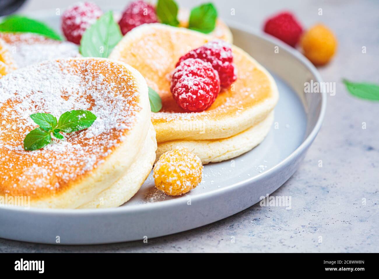 Crêpes japonaises moelleuses aux framboises dans une assiette grise, fond gris. Concept de cuisine japonaise. Banque D'Images