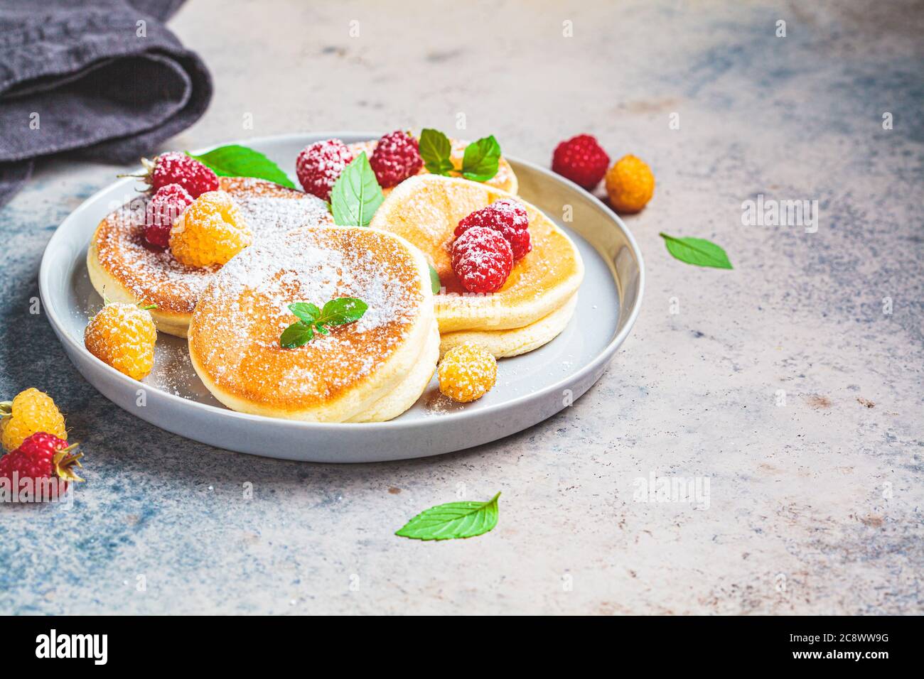 Crêpes japonaises moelleuses aux framboises dans une assiette grise, fond gris. Concept de cuisine japonaise. Banque D'Images