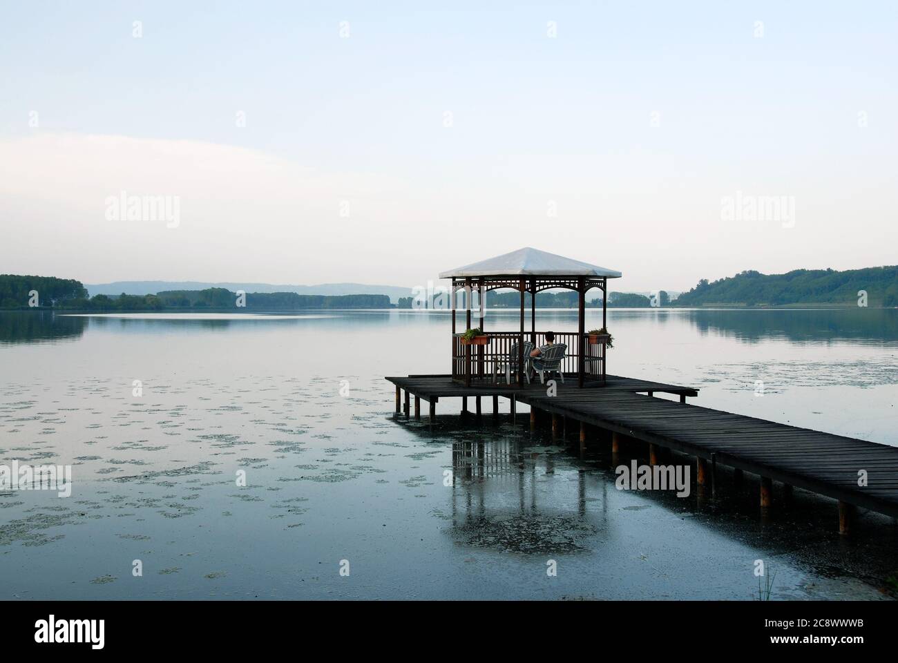 Personne assise sous un belvédère sur un quai au bord du lac lors d'une soirée de printemps Banque D'Images