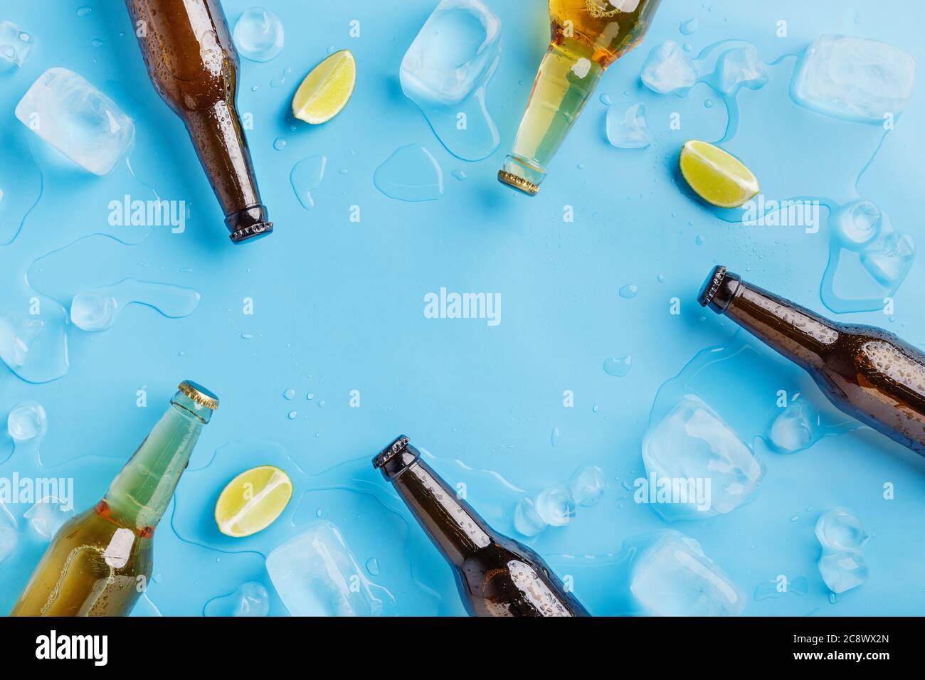 Bouteilles de bière en verre foncé et clair sans étiquette avec glace et morceaux de chaux sur fond bleu Banque D'Images