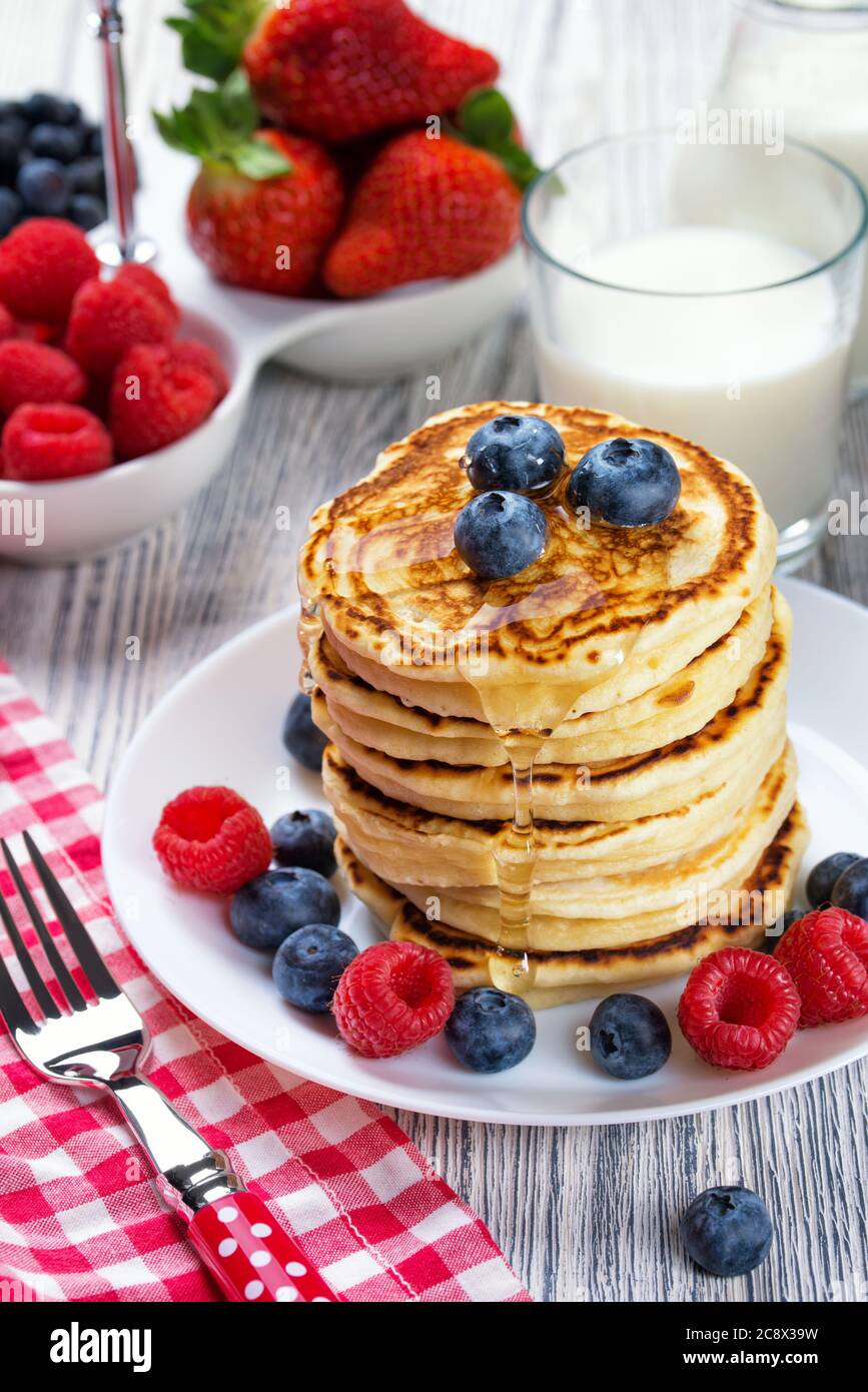 Pile de crêpes aux myrtilles fraîches et à la framboise, versée avec du miel. Lait et baies fraîches, concept de petit déjeuner sain Banque D'Images