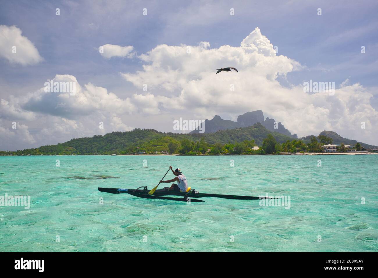 Bora Bora, Tahiti, Polynésie française. Un garçon local pagaie un canot moderne en saillie dans de l'eau claire translucide. Monter Otemanu ou Temanu en arrière-plan Banque D'Images