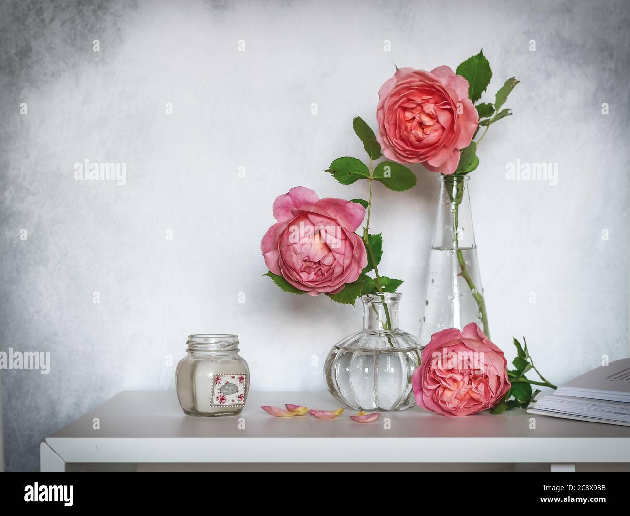 Roses roses dans de petits vases en verre et une bougie sur une étagère Banque D'Images