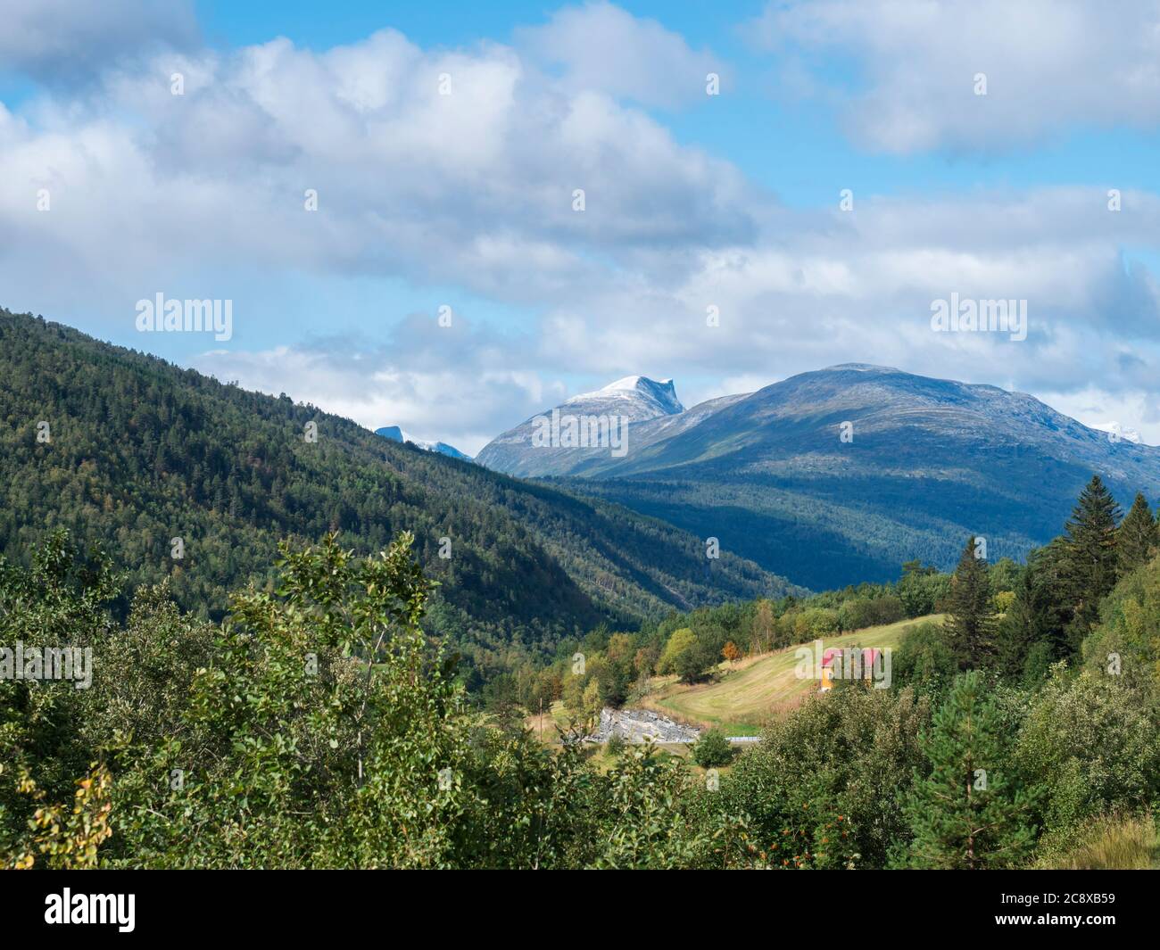 Vue sur la vallée de Romsdalen depuis la route E136 avec des sommets enneigés de montagnes, forêt verte et petite maison jaune rouge. Ciel bleu nuages blancs Banque D'Images