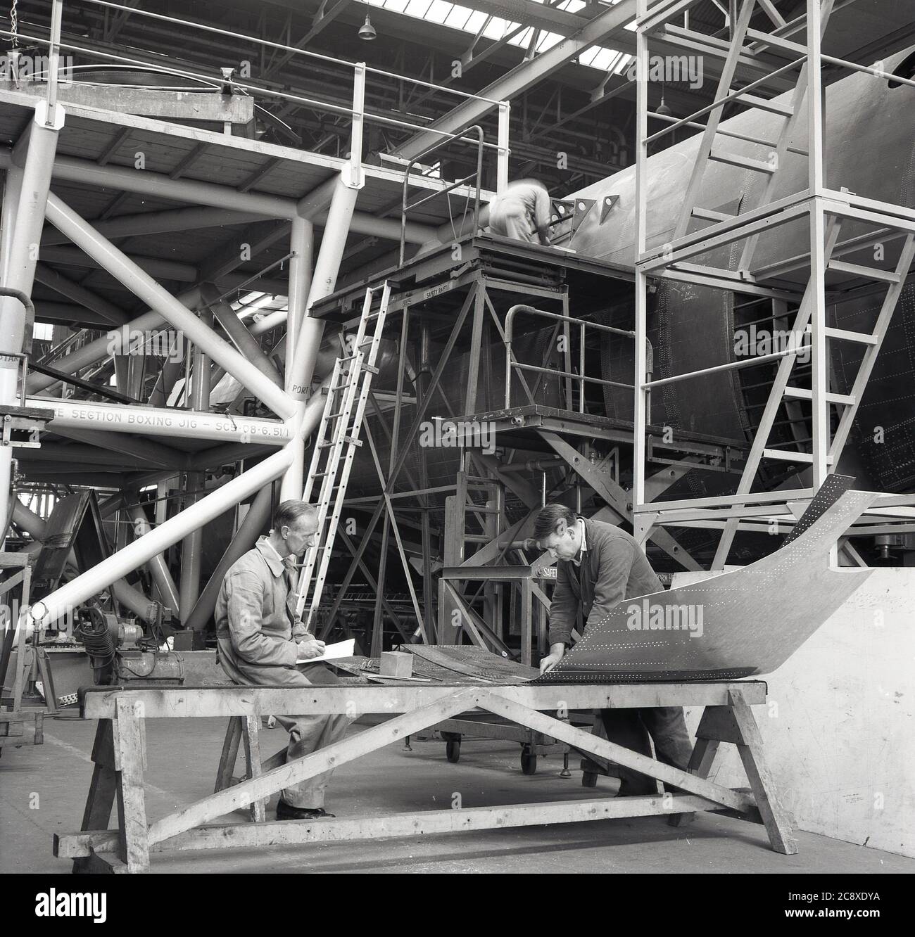 Années 1950, historique, deux ingénieurs chez un constructeur aéronautique dans un grand cintre vérifiant un panneau d'acier externe pour le fuselage ou le corps principal d'un gros avion en construction, Belfast, Irlande du Nord, Royaume-Uni. Banque D'Images