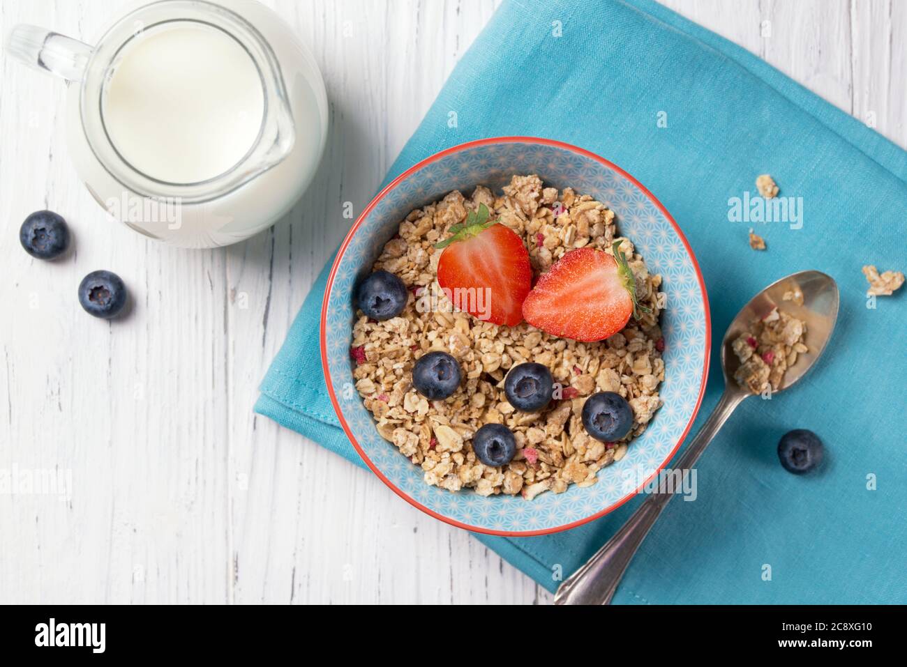 Petit déjeuner sain, bol avec muesli de granola avec fraise et myrtille et pot à lait, fond en bois, vue du dessus Banque D'Images