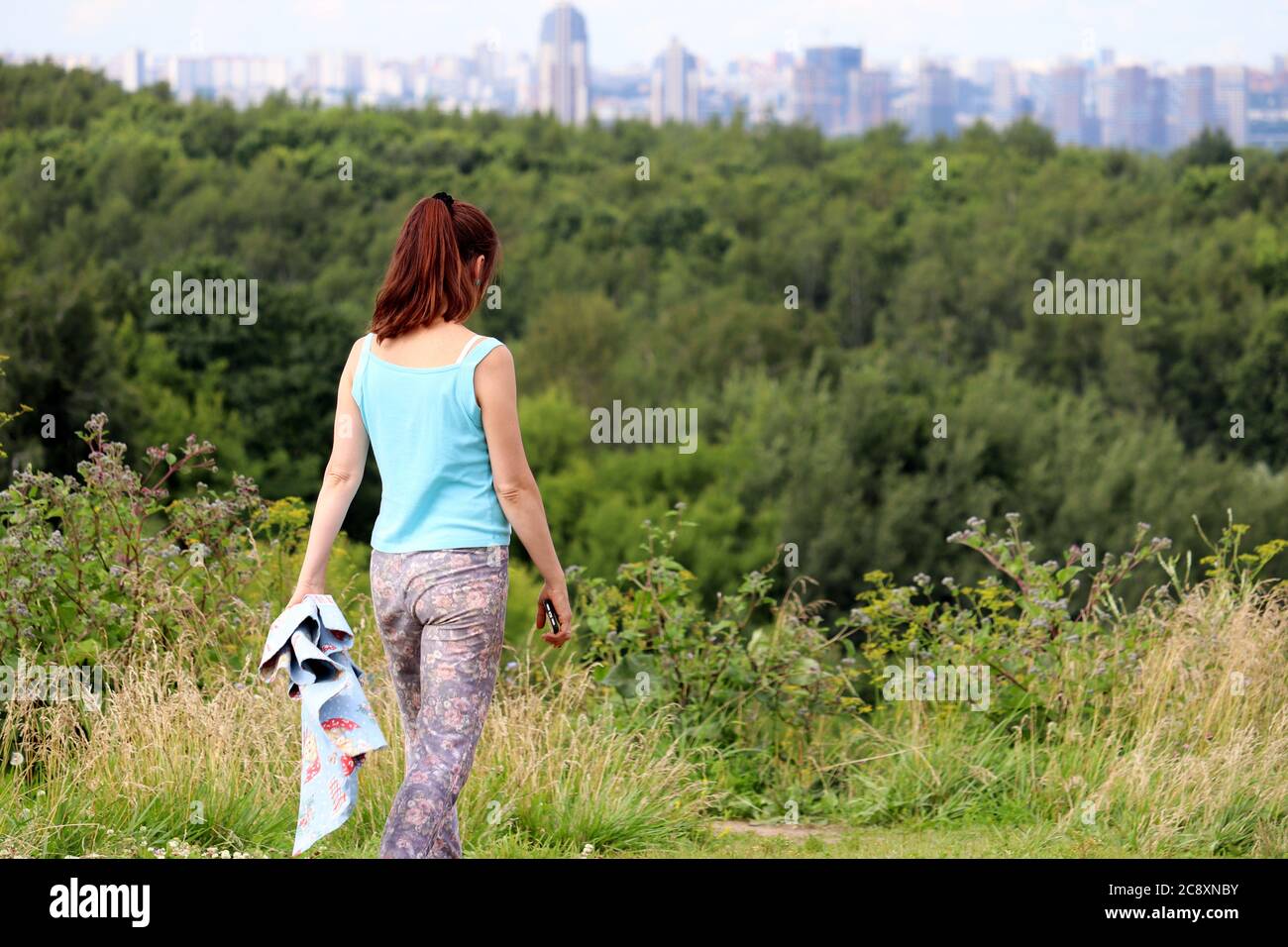 Fille avec un smartphone marchant dans un parc sur fond de ville. Loisirs d'été et randonnée Banque D'Images