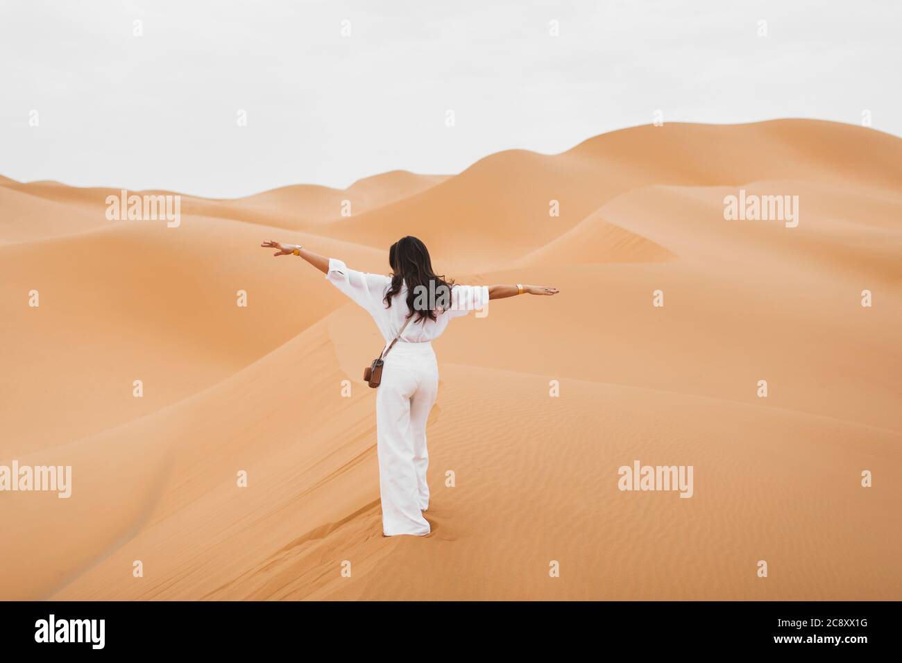 Femme en chemise blanche élégante et pantalon avec photo rétro heureux d'explorer les dunes de sable du désert du Sahara au Maroc. Vue de l'arrière. Banque D'Images