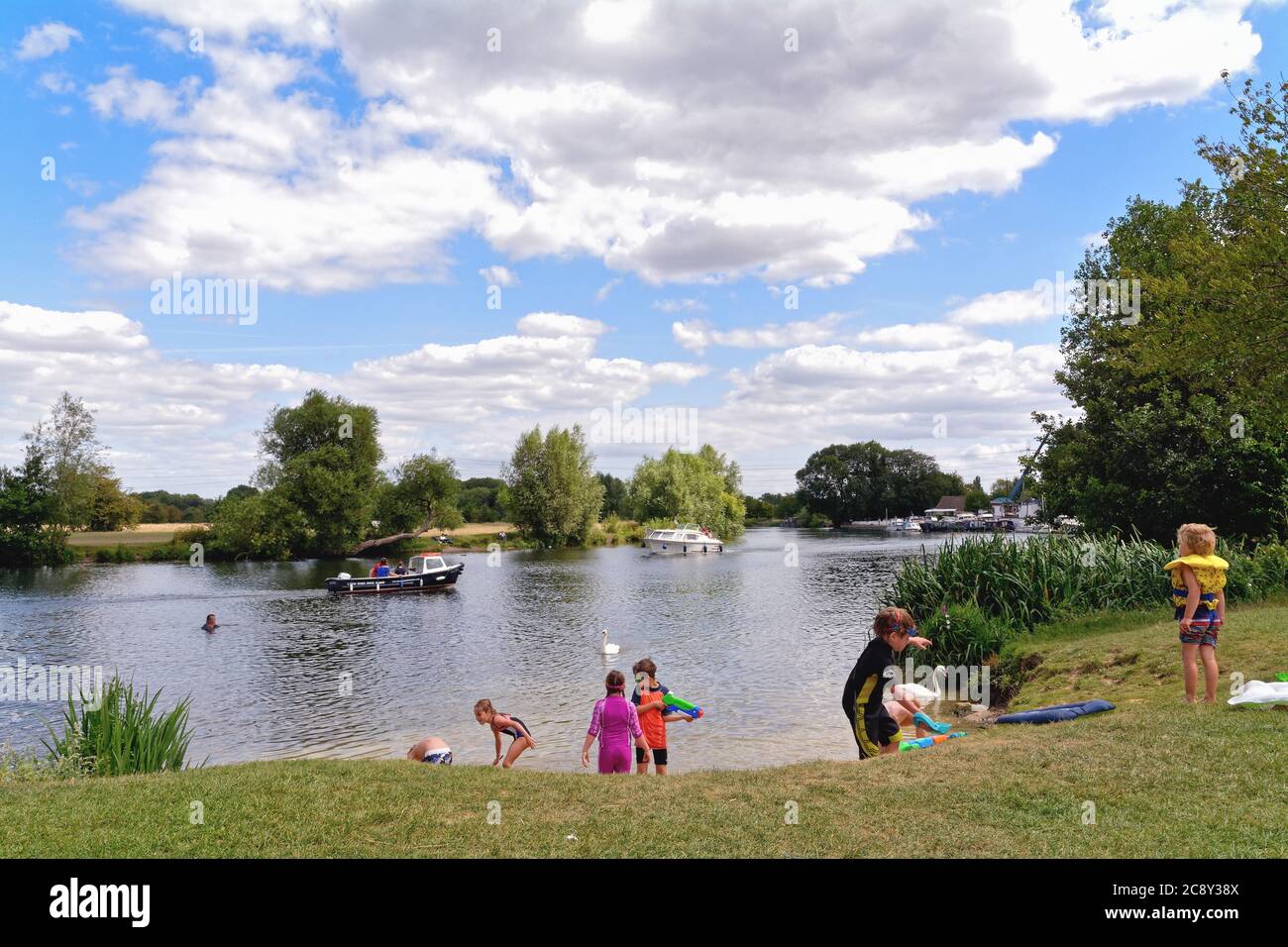 La Tamise à Chertsey avec des enfants jouant sur le remblai le jour de l'été avec des bateaux fluviaux qui naviguent en arrière-plan, Surrey Angleterre Royaume-Uni Banque D'Images