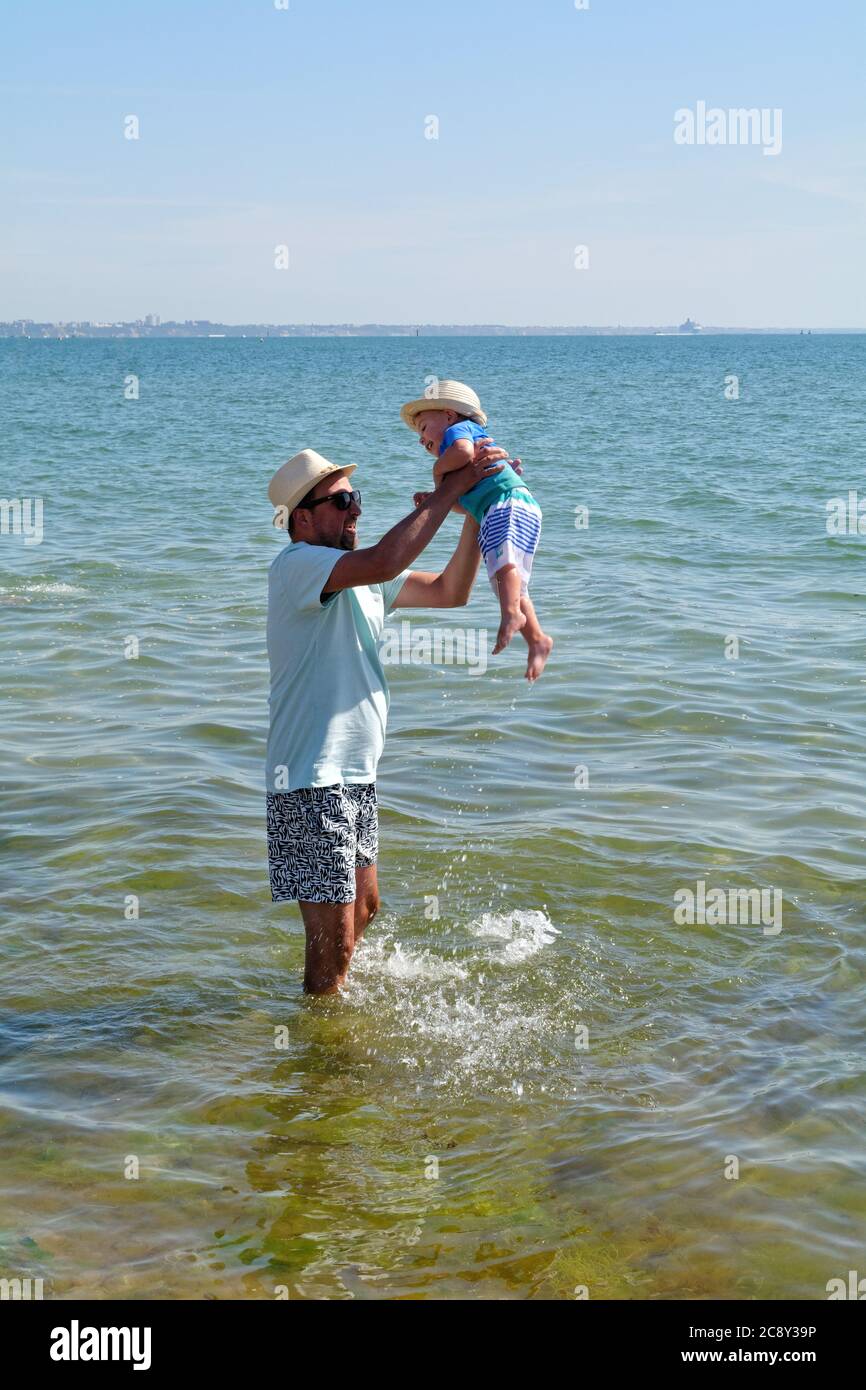 Un père et un fils tout-petits debout sur le bord de l'eau à la plage de Studland Bay, un jour d'été chaud, Dorset Angleterre Royaume-Uni Banque D'Images