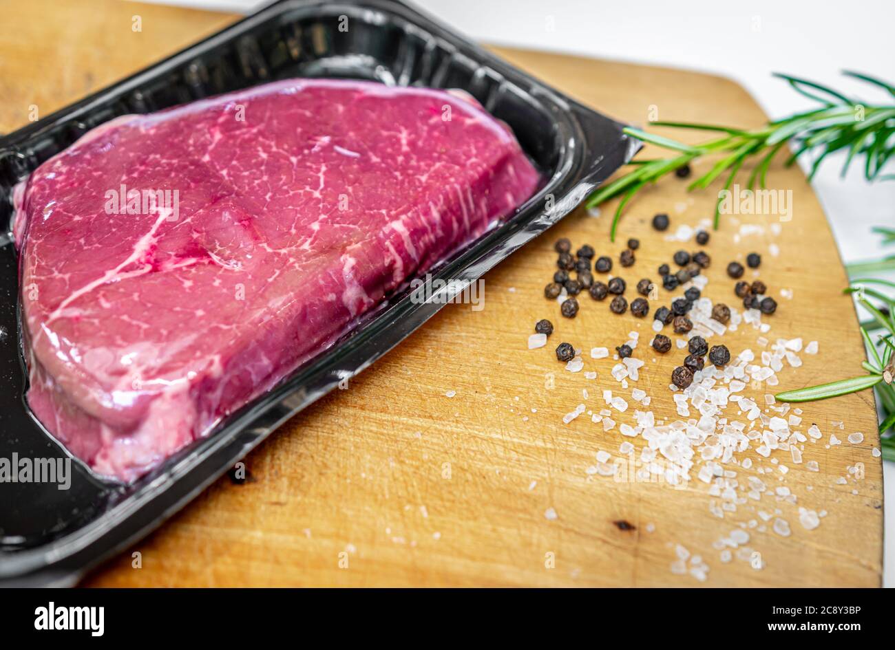 Steak de bœuf dans un emballage sous vide et épices sur planche à découper en bois avec espace d'imitation Banque D'Images