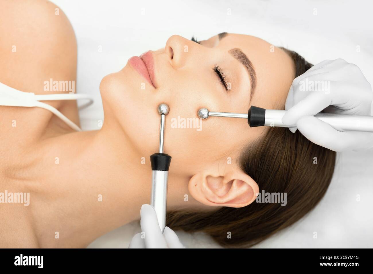 Femme obtenant la procédure de micro-courant facelift. Esthéticienne faisant anti-âge, pour effectuer le serrage facial et la tonification. Banque D'Images