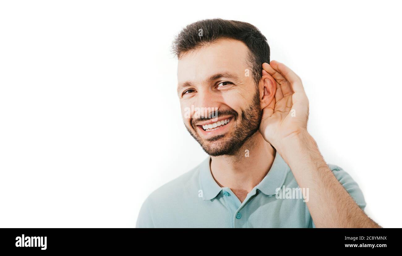 Vérifiez votre audition. L'homme de race mixte positif tient sa main près de son oreille, isolé sur un fond blanc. Santé de l'oreille, traitement et diagnostic de la coroin Banque D'Images