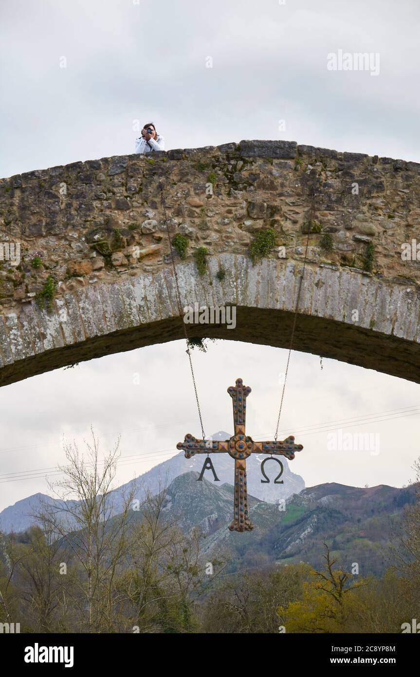 Photographe sur le pont de pierre appelé à tort pont romain avec sa Cruz de la Croix de Victoria qui y pend (Cangas de Onís, Asturies, Espagne) Banque D'Images