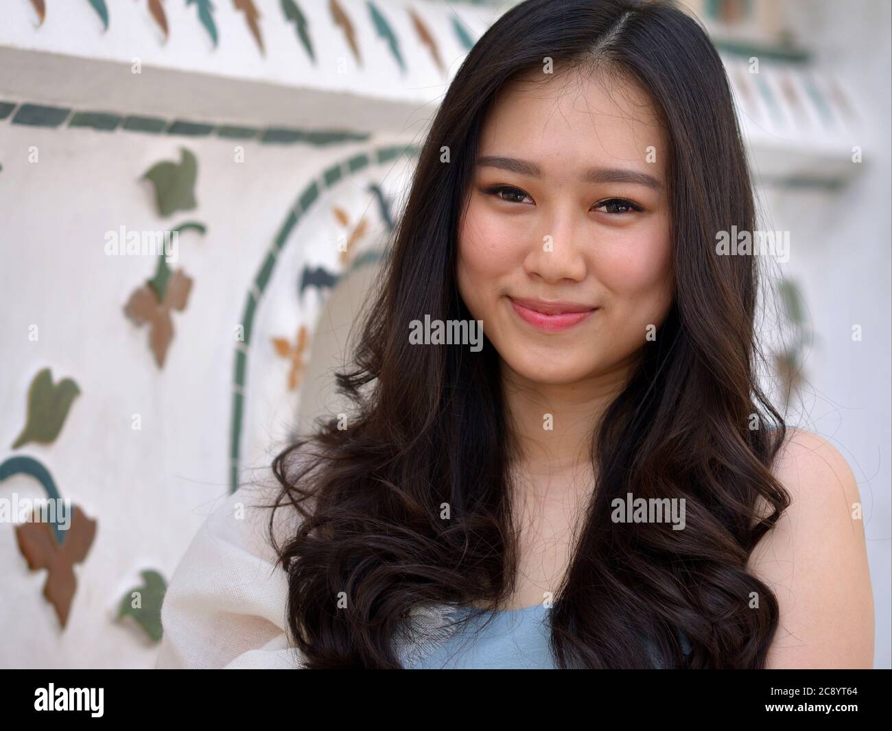 Une jolie fille du Sud-est asiatique aux cheveux longs aux extrémités courbées pose pour la caméra au temple Wat Arun de Bangkok. Banque D'Images