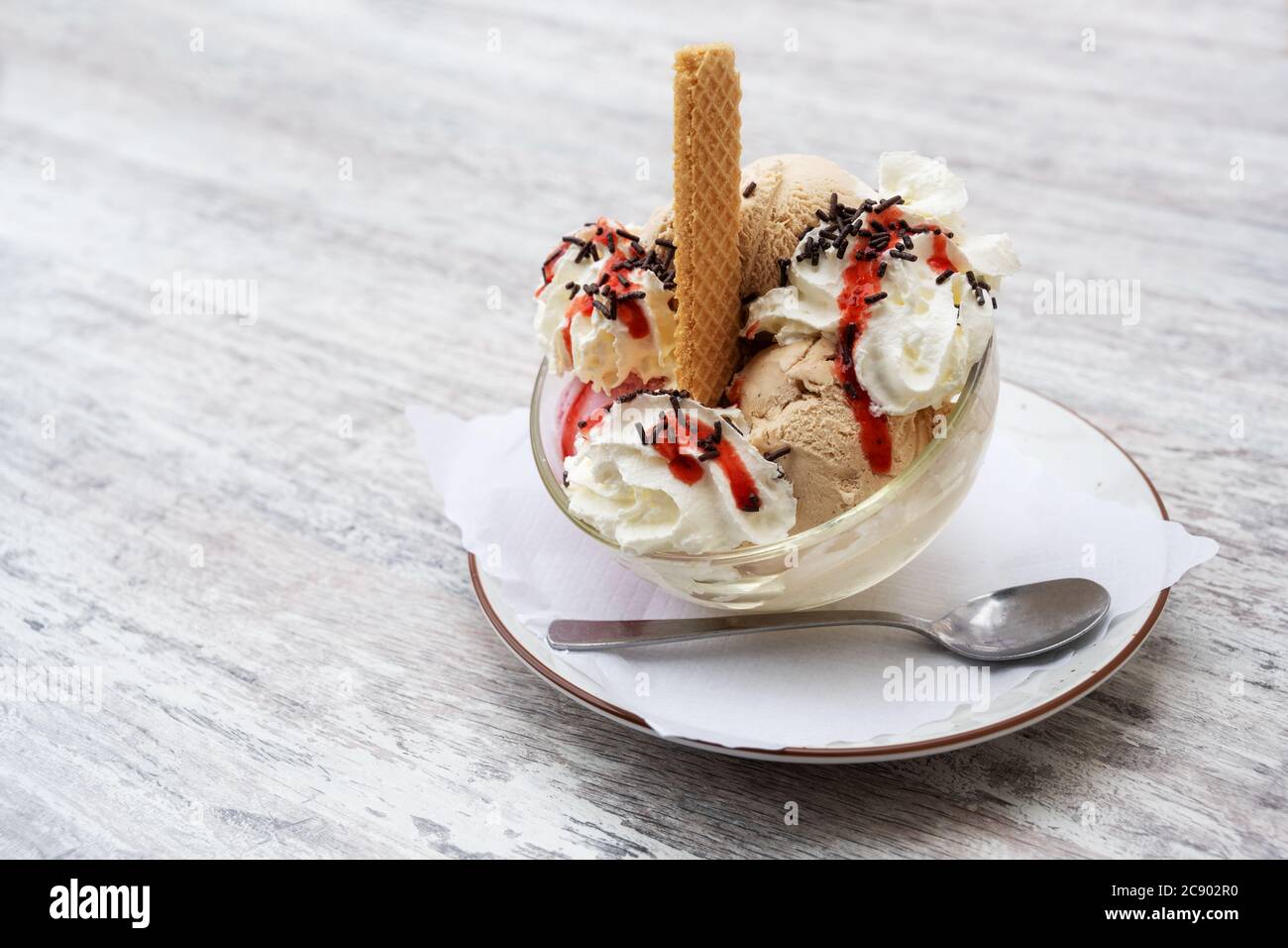 Sundae avec des boules de glace, de la crème fouettée, de la sauce aux fruits rouges et des saupoudrés de chocolat dans un bol en verre sur une table grise, espace pour les copies, sélection, narr Banque D'Images