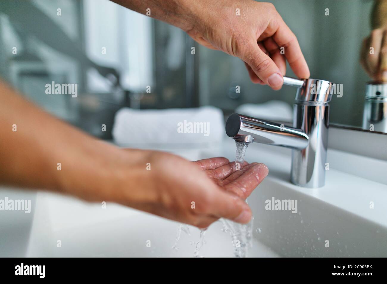 Homme se lavant les mains dans l'évier de salle de bains à la maison en vérifiant la température en touchant l'eau courante avec la main. Fermez les doigts sous l'eau chaude hors d'un robinet Banque D'Images