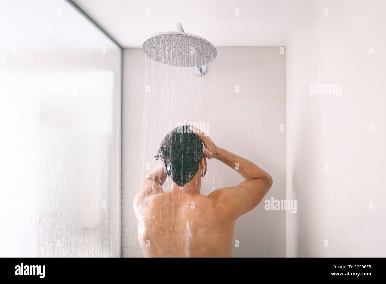 Homme prenant une douche se lavant les cheveux avec le produit de shampooing sous l'eau tombant de la tête de douche de pluie de luxe. Petit matin, hôtel de luxe style de vie Banque D'Images