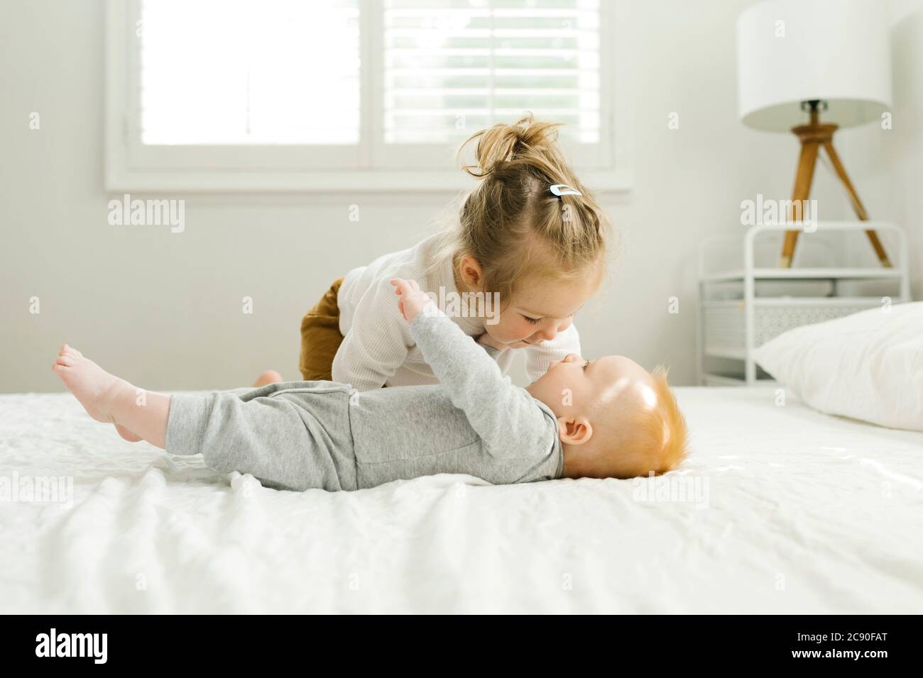 Petite sœur embrassant son bébé frère sur le lit Banque D'Images