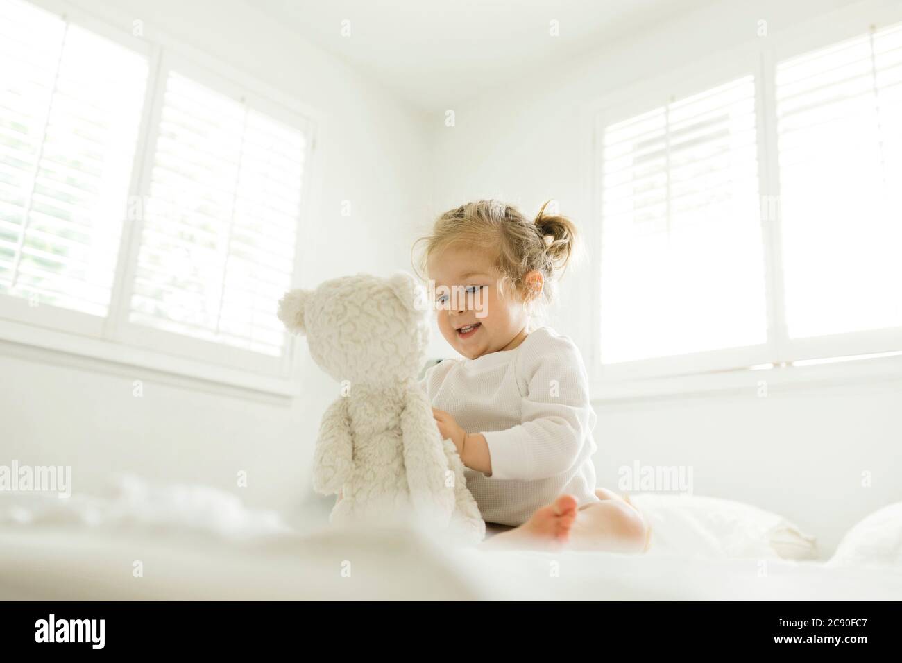 Petite fille jouant au lit avec son jouet ours en peluche Banque D'Images