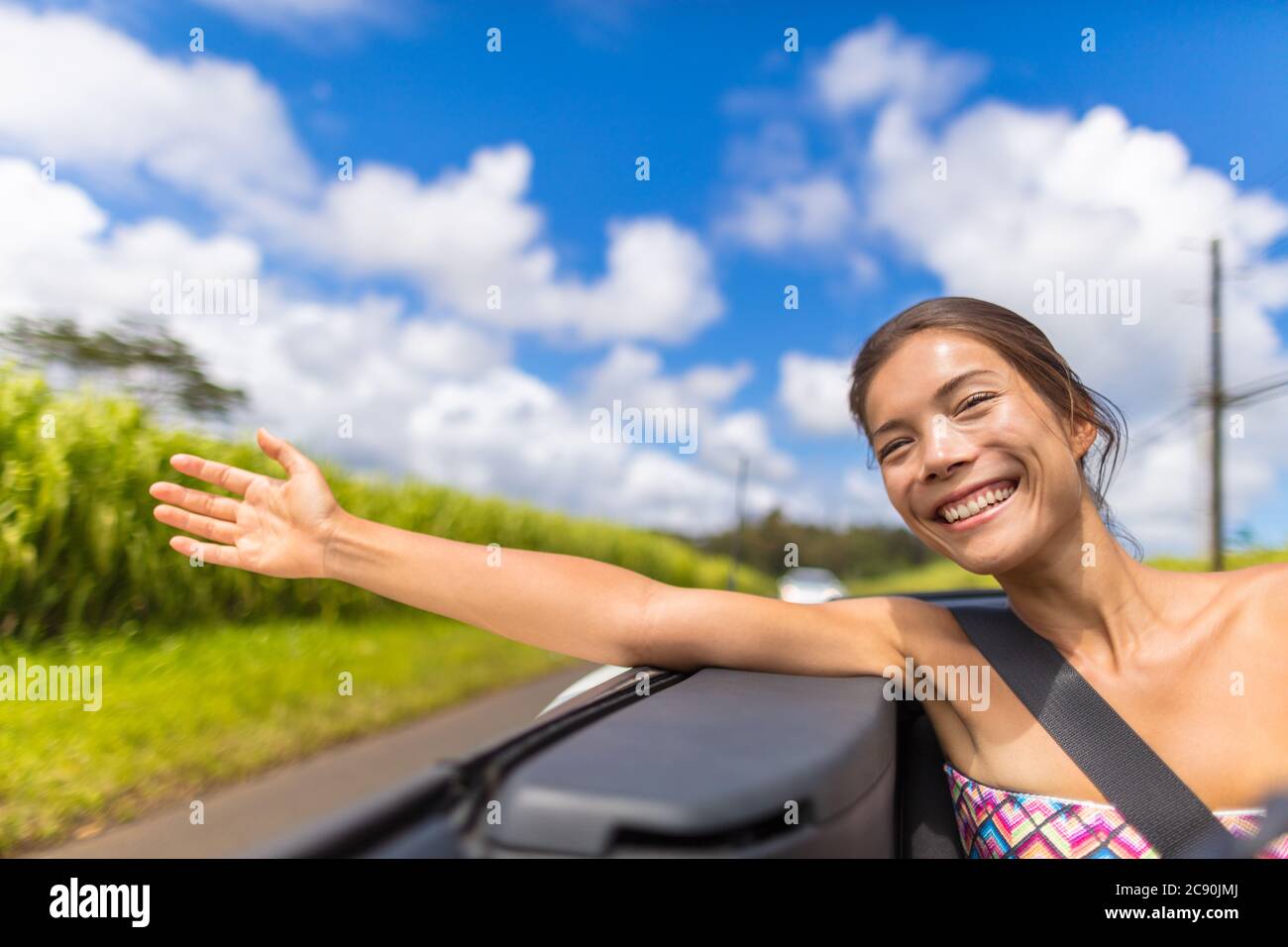 Voiture Road trip femme liberté avec la main flottant dans le vent. Fille asiatique assis dans une voiture convertible sans souci profiter de vacances de voyage avec bras Banque D'Images