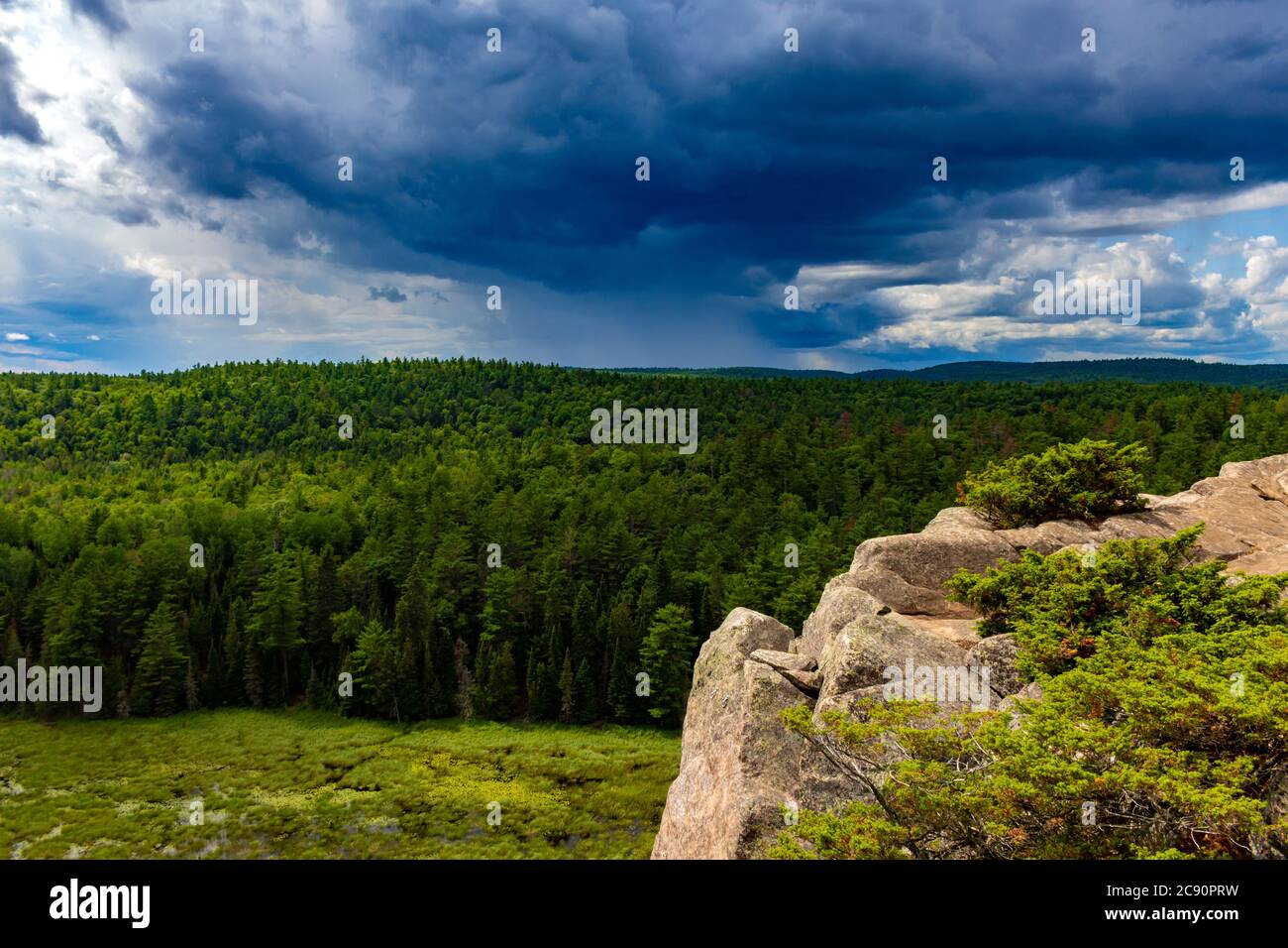 Un ciel nuageux s'étend vers l'horizon avec des pluies lointaines tombant au-dessus d'une forêt d'arbres verts. Les bois sont vus d'en haut avec une cli rocheuse Banque D'Images
