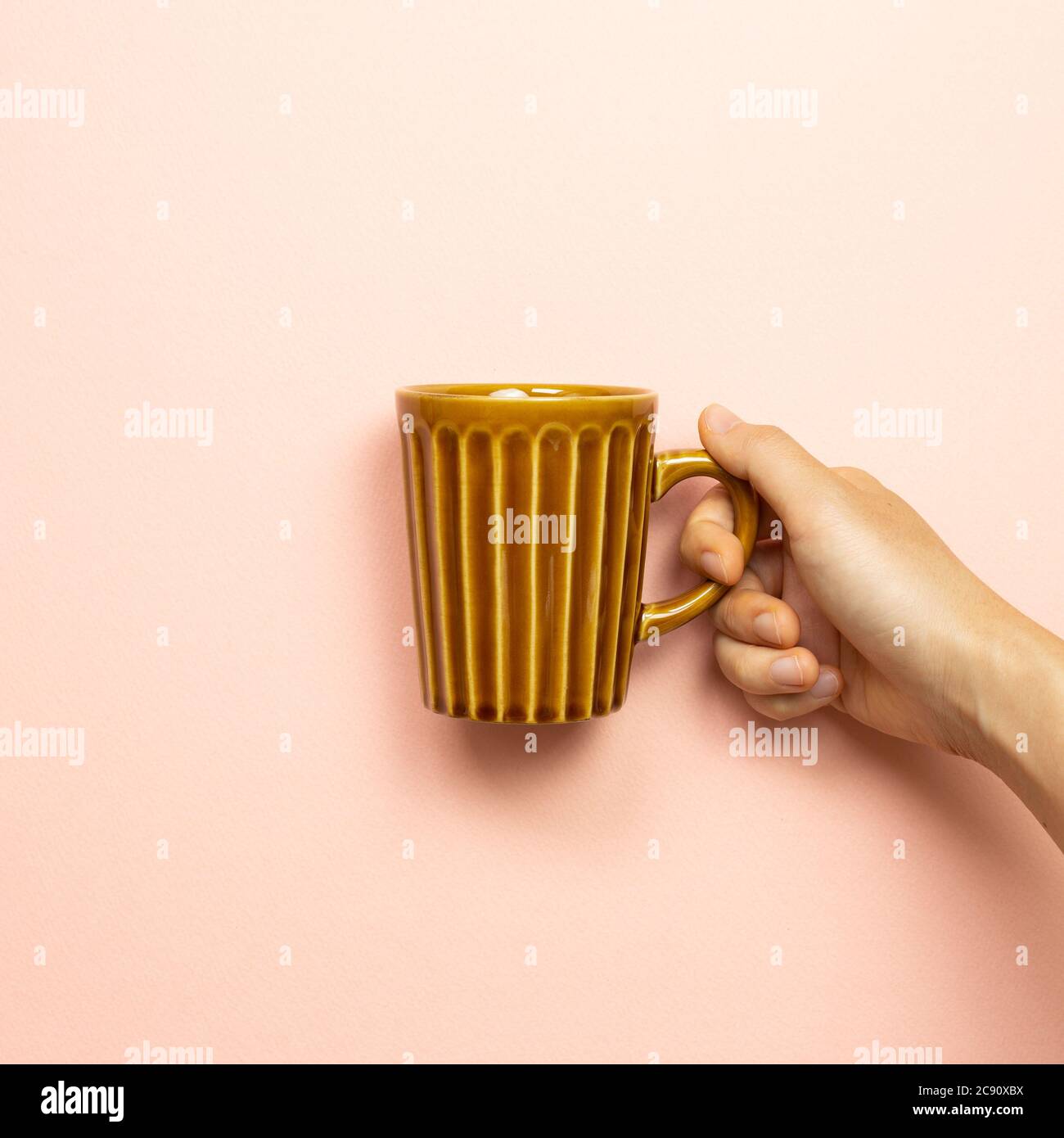 Main femme tenant une tasse vide brune sur fond rose Banque D'Images