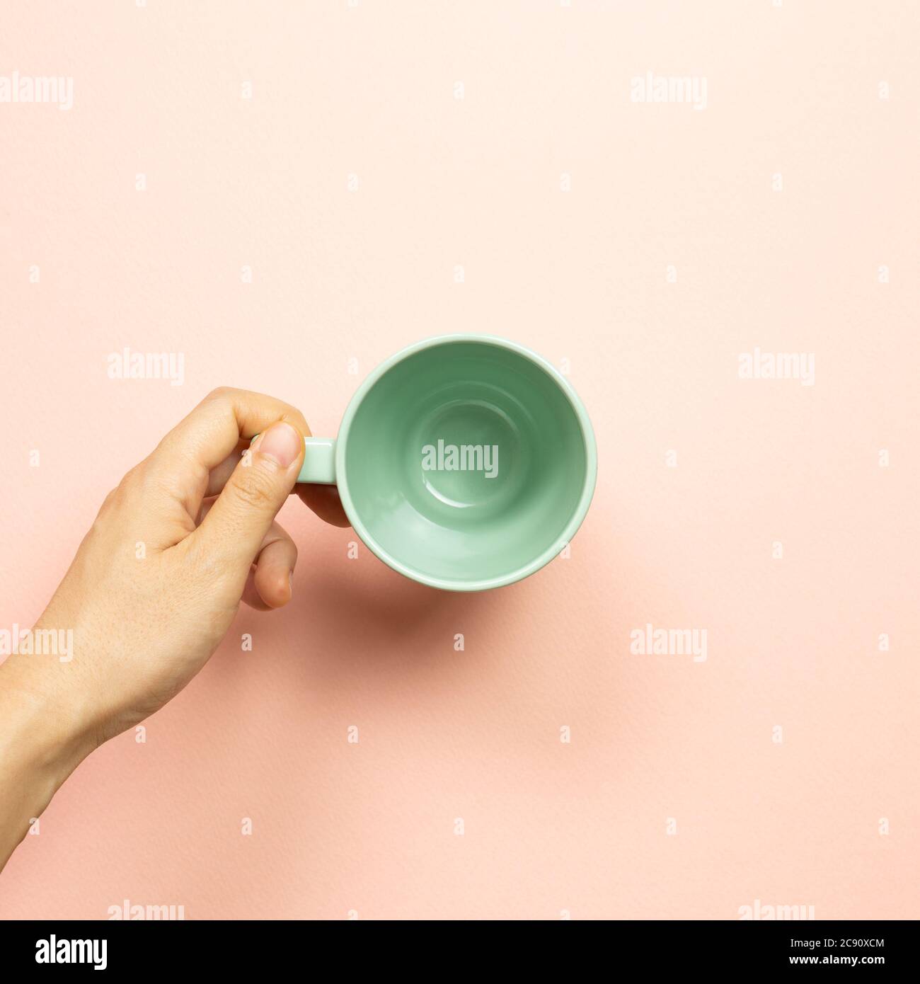 Femme main tenant une tasse vide verte sur fond rose. Vue du dessus Banque D'Images