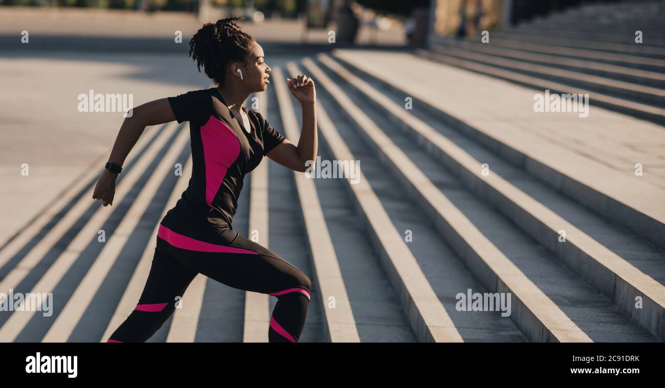 Course matinale. Une jeune fille afro-américaine avec casque sans fil et tracker de forme physique passe les escaliers Banque D'Images