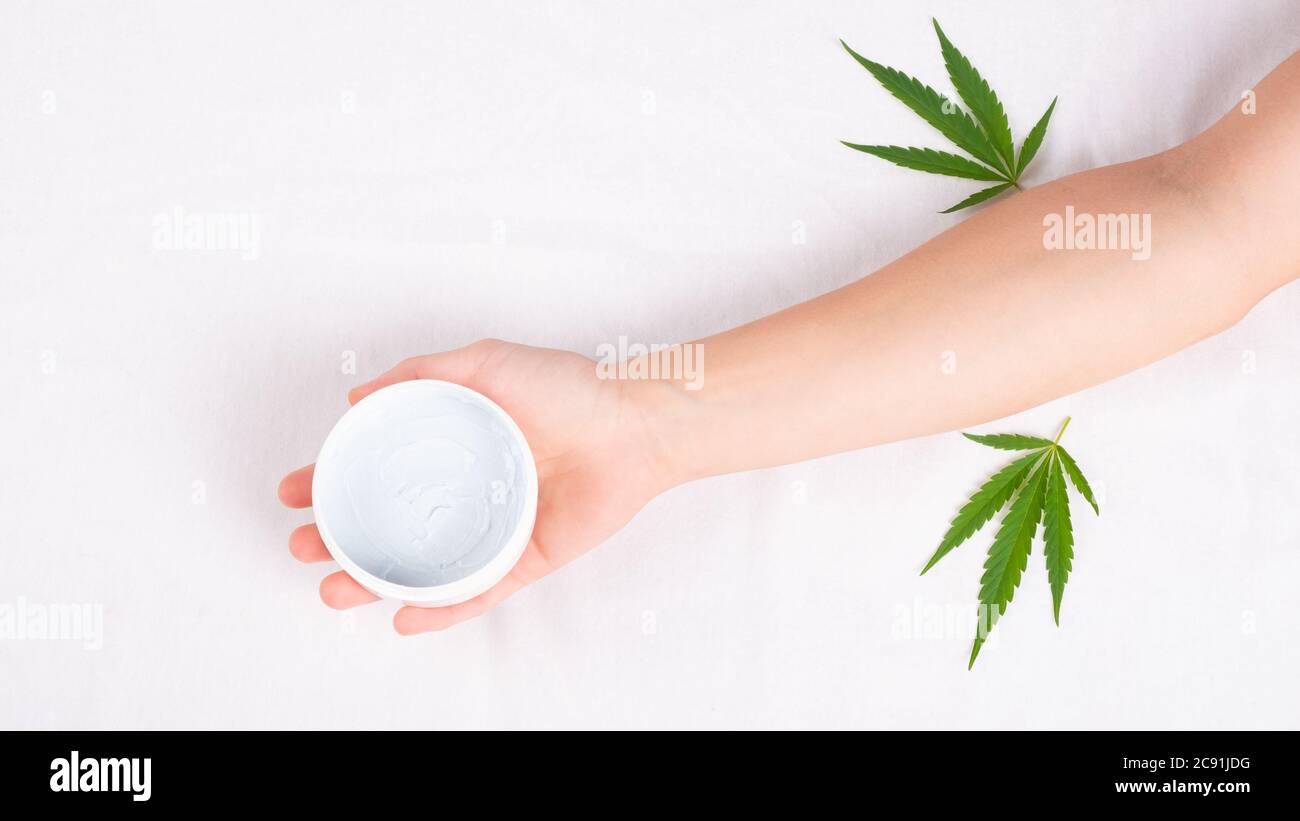 beauté, spa, soins de la peau cosmétiques avec extrait de marijuana. pot blanc de crème à la main avec feuille de cannabis verte sur fond blanc. Banque D'Images